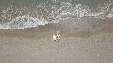 Couple resting on sand near waving seaの写真素材