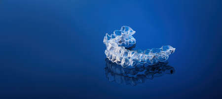 Invisible orthodontics cosmetic brackets on blue gradient background, tooth aligners, plastic braces. A way to have a beautiful smile and white teeth.の写真素材