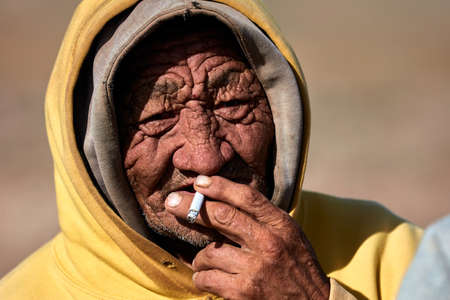 An elderly, wrinkled man smokes. Mongol in modern clothing. 09/07/2019. Gobi Desert, Mongolia.のeditorial素材