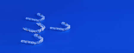 Invisible orthodontics cosmetic brackets on blue background, tooth aligners, plastic braces. A way to have a beautiful smile and white teeth.の写真素材