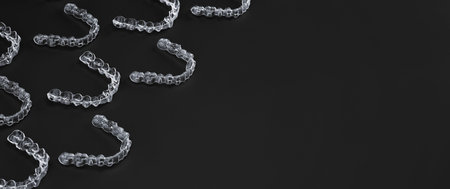 Invisible orthodontics cosmetic brackets on black background, tooth aligners, plastic braces. A way...