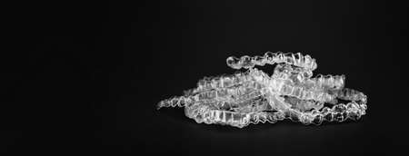 Invisible orthodontics cosmetic brackets on black background, tooth aligners, plastic braces. A way to have a beautiful smile and white teeth.の写真素材