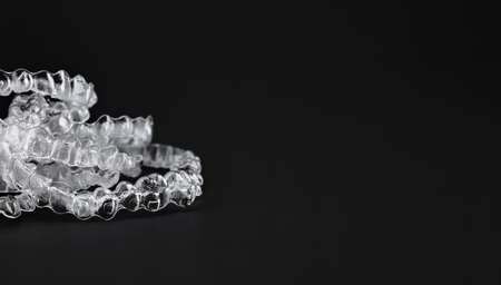 Invisible orthodontics cosmetic brackets on black background, tooth aligners, plastic braces. A way to have a beautiful smile and white teeth.の写真素材