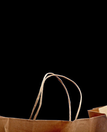 Blank brown paper carrier bag with handles for shopping. Paper bag on a black background,...