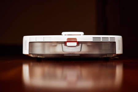 Smart Robot Vacuum Cleaner on wood floor. Robot vacuum cleaner performs automatic cleaning of the apartment at a certain time. Smart home.の写真素材