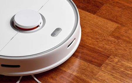 Smart Robot Vacuum Cleaner on wood floor. Robot vacuum cleaner performs automatic cleaning of the...