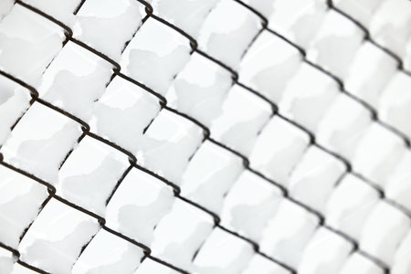 Snow on a mesh fence close-up, snow fence. Abstract winter background. Snow on a wire fence