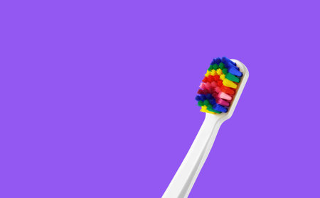 Fancy toothbrush with multicolored bristles on royal purple background. Bristles in all colors of the rainbow. Rainbow toothbrush with white knob. Fashionable oral careの写真素材