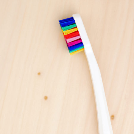 White toothbrush with multicolored bristles on a wooden table. Bristles in all colors of the rainbow. Rainbow toothbrush with white knob. Fashionable oral careの写真素材