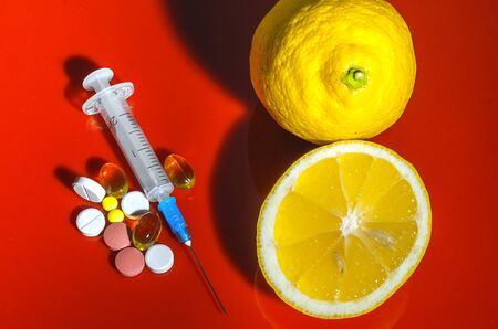 Lemons on a red background with syringes and pills. Medical preparations and vitamin C. Subcutaneous injectors with tablets side by side with lemons on a red backgroundの写真素材