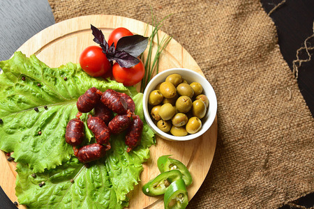 Hunting sausages on a wooden board with lettuce, basil, cherry tomatoes, paprika and olives.の写真素材
