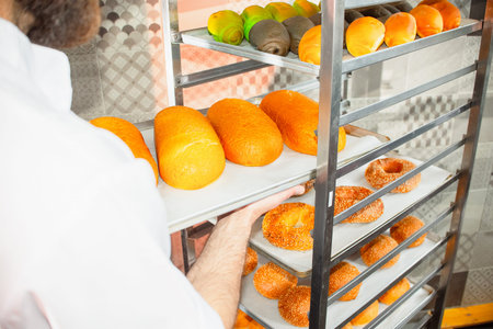 A young handsome baker takes out hot fresh baking from the oven in the bakery.