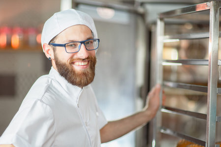 Portrait of a young beautiful baker with fresh bread and an oven in the background.