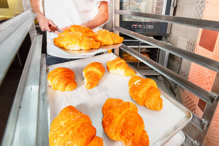 The baker keeps hot fresh croissants against the backdrop of the oven. Croissants close-up.
