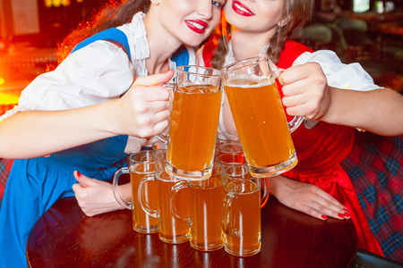 Young beautiful girls clink glasses with beer at the Oktoberfest festival.の写真素材