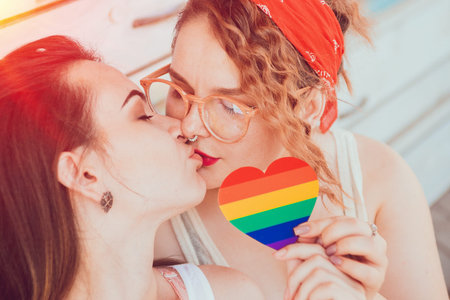 A young lesbian couple kissing and holding a heart with the flag of LGBT