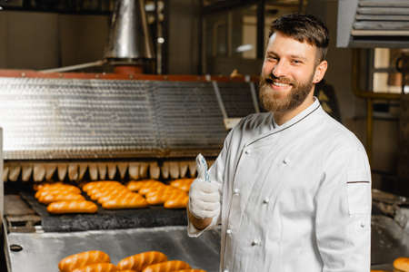 Portrait of a young baker on the background of an industrial oven in a bakery. Industrial bread productionの写真素材