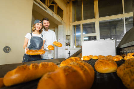 Girl and man bakers with bread in their hands against the background of an industrial oven in a bakery. Industrial bread productionの写真素材