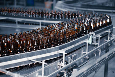 Glass beer bottles of brown color on the conveyor line of beer bottling close upの写真素材