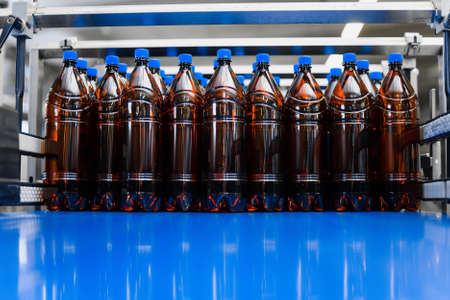 A row of plastic beer bottles on a conveyor belt. Industrial production of beer. Beer bottles mockupの写真素材