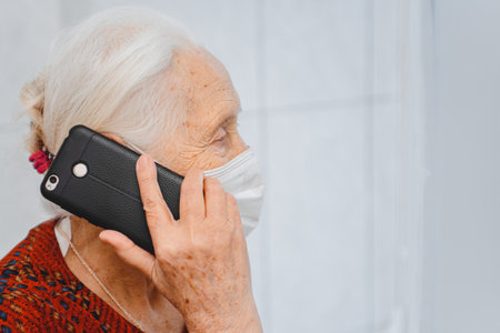 Elderly woman in protective medical mask talking on a mobile phone.の写真素材