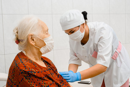 Elderly woman getting vaccine. Doctor vaccinates an elderly woman wearing a surgical maskの写真素材