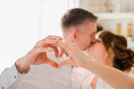 Young happy couple kissing and making heart shape with hands while demonstrating wedding ringsの写真素材
