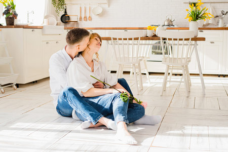 Romantic young couple kissing while sitting on the floor in the kitchenの写真素材