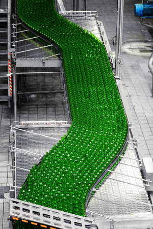 Automated conveyor line in a brewery. Rows of green glass bottles on a conveyor belt. Industrial...
