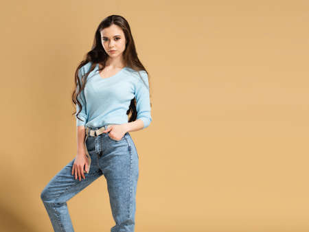 Young beautiful girl with long curly hair in a blue sweatshirt and blue jeans on a pastel orange studio background. Sweatshirt mockupの写真素材