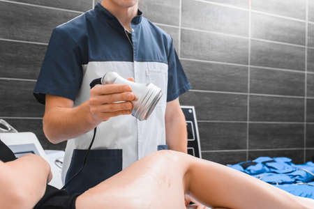 The doctor holds the ultrasound massage apparatus over the patient's leg.の写真素材