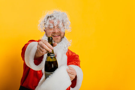 Drunk santa takes out a bottle of champagne from his hat on a yellow isolated backgroundの写真素材
