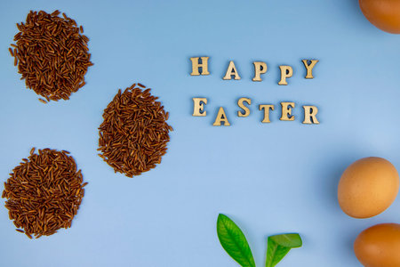 top view of the inscription from wooden letters happy easter, eggs from unpolished brown rice and...