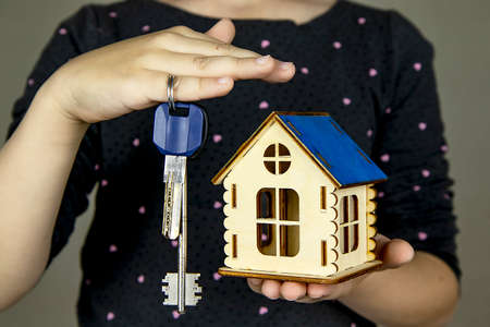 Close-up of a hand holding keys and a model of a wooden house. The concept of real estate sale, mortgage, rental housing.の写真素材