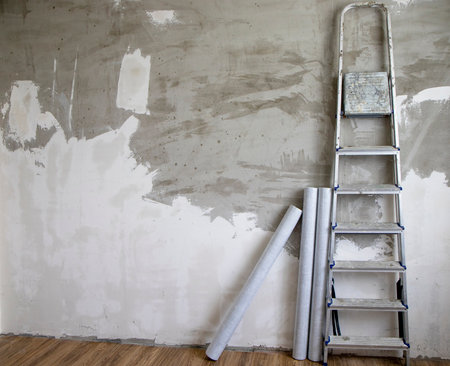 side view of a stepladder and rolls of non-woven wallpaper against a gray concrete wall, sometimes covered with white putty. The concept of renovation and repairの写真素材