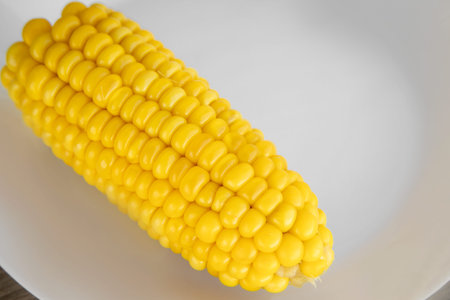 a view of delicious juicy yellow boiled corn on a white plate on the side. Healthy cereals in the...