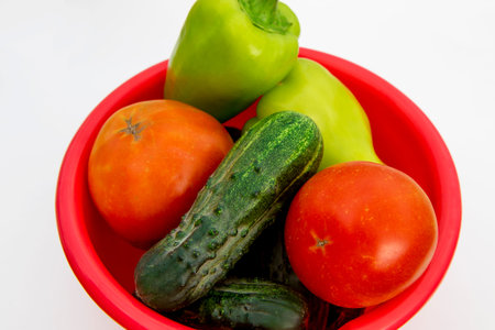 A large red saucepan with vegetables. Tomatoes, cucumbers and peppers. isolated on a white background. Seasonal plant vitaminsの写真素材