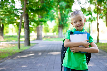 back to school. Portrait of an elementary school student. First grader. The beginning of classes. A child boy with a backpack holds textbooks and a notebook in his hands and smiles.Copy spaceの写真素材