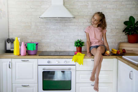 A girl-child sits on a table and smiles broadly looking at the working inventory after finishing cleaning the house The concept of helping parents with household choresの写真素材