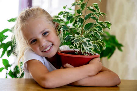 A cute little gardener girl hugs a pot of focus and smiles. Home gardening, love of indoor plants.の写真素材