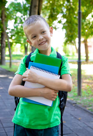 back to school. Portrait of an elementary school student. First grader. The beginning of classes. A child boy with a backpack holds textbooks and a notebook in his hands and smilesの写真素材