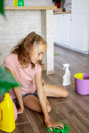 Cleaning the room. Selective focus on A baby girl is sitting on the floor, washing and cleaning the house with detergents. Cleanliness and order.の写真素材