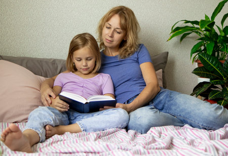 A pretty young mother is reading a book with her daughter. The concept of a happy loving family, family leisure and educationの写真素材