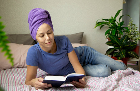 a young woman with a towel on her head is lying in bed and reading a book. The concept of rest, education and time for yourselfの写真素材
