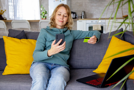 a young woman makes a payment sitting on the sofa with a laptop and a credit card, she orders goods, uses the services of an Internet bank. Online shopping, seasonal sales, Black Friday conceptの写真素材