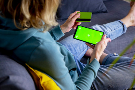 a woman makes a payment sitting on the couch with a smartphone and a credit card, she orders goods, uses the services of an Internet bank. Online shopping, Black Friday concept. Green screenの写真素材