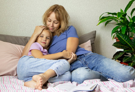 Happy loving family. A mother and her girl daughter hug each other while lying in their bed. The concept of love, tenderness and careの写真素材