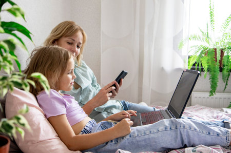 A pretty young woman and her daughter use a laptop at home watching videos, movies or cartoons while lying on the bedの写真素材