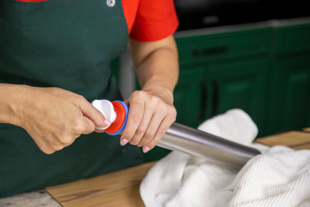 View of a pastry chefs woman in red and green work clothes. She twists a modern metal rolling pin before rolling out the baking doughの写真素材
