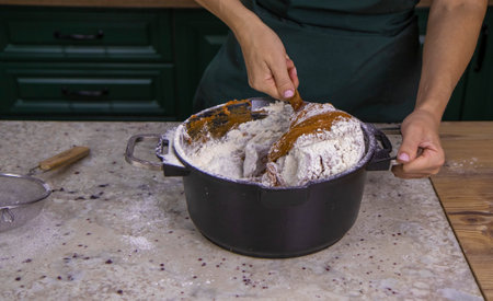 A view of the hands of a female pastry chef kneading dough in a metal saucepan with a wooden spoon. The concept of cooking and baking gingerbread, cookies, dessertsの写真素材